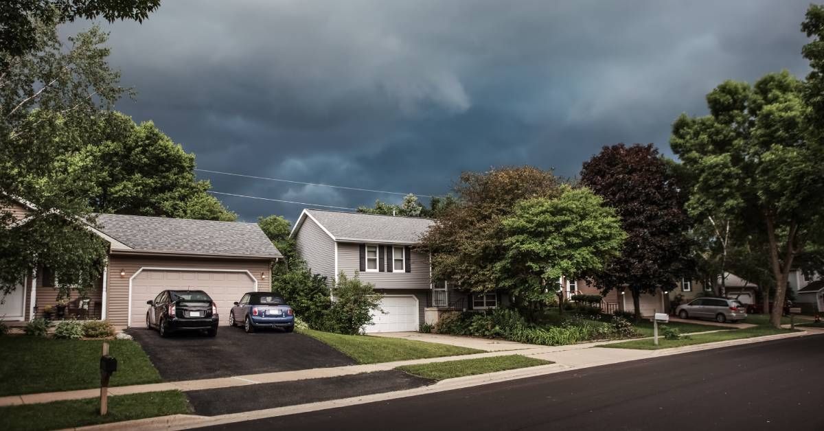 A suburban street with neutral-colored homes and a sky covered in grey clouds before a thunderstorm.