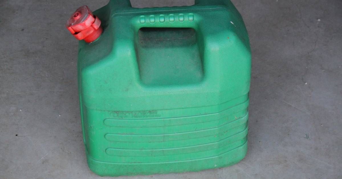 A green plastic fuel can with a top handle and a red twistable cap sits on a concrete surface.