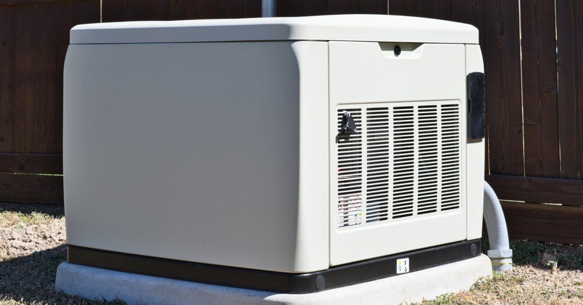 A white rectangular generator with an exhaust panel is sitting on a concrete slab in a yard with bro