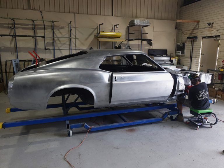 Silver car body on a blue frame in a workshop, with tools and equipment around it.