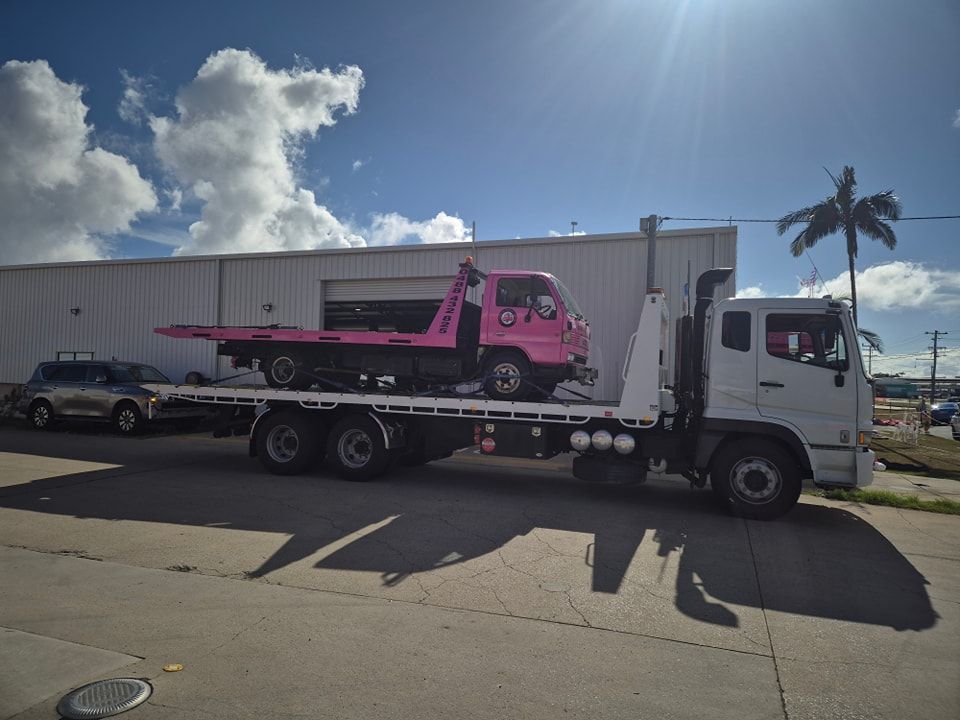 A Pink Tow Truck With A Car On The Back Is Parked In Front Of A Building — M8S Rates Mechanical In Gladstone Central, QLD