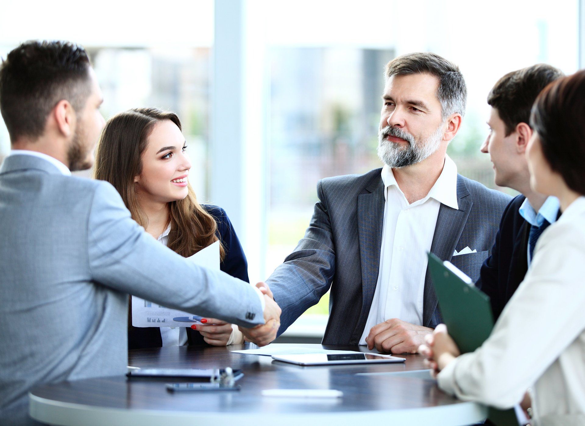 A group of business people are sitting around a table shaking hands.