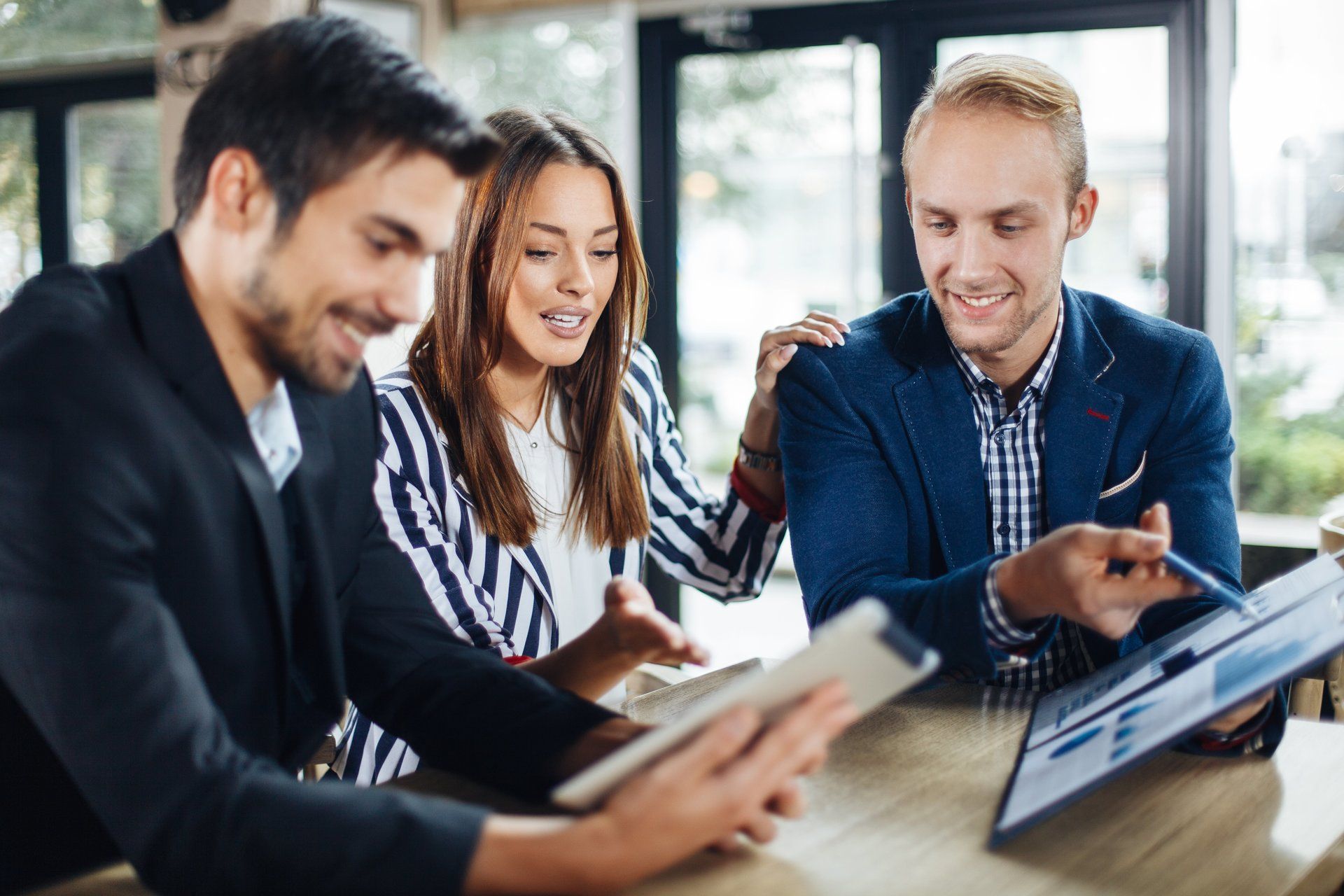 A group of people are sitting at a table looking at a tablet.