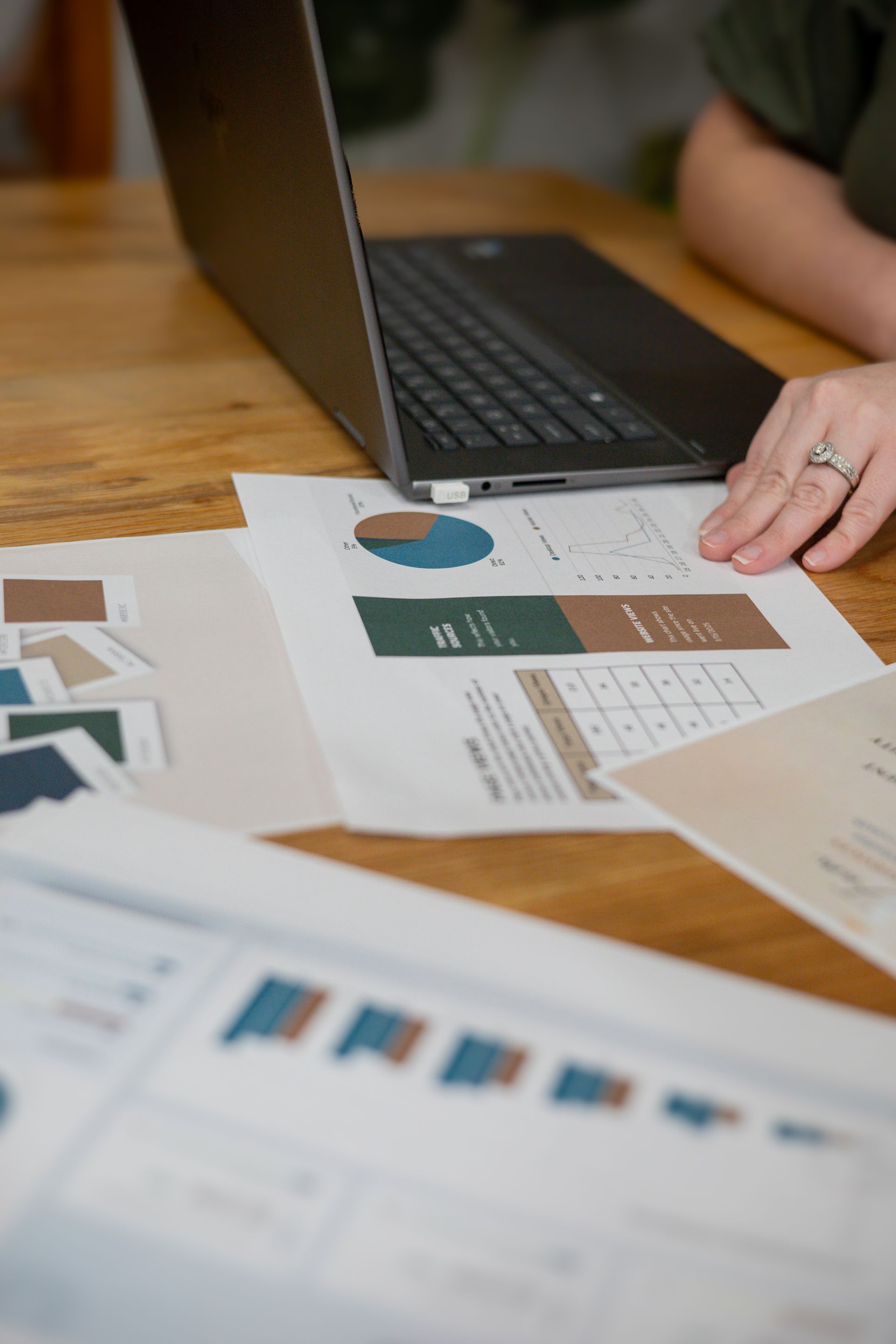 Person working on laptop at a wooden table, surrounded by charts and graphs.