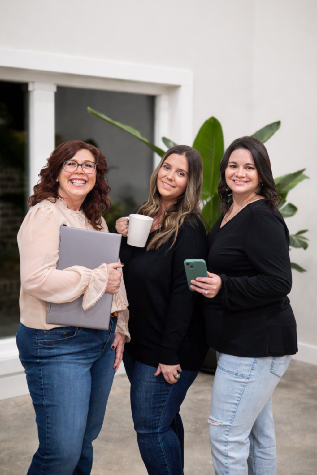 Woman in glasses smiles, sitting in brown chair at a desk, with floral wallpaper background.