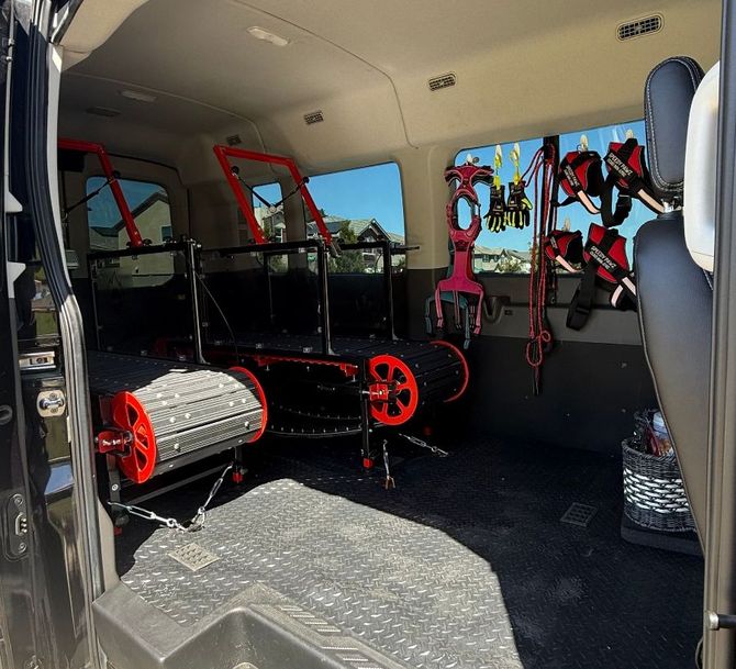 Inside a van: Two treadmills, equipment hanging on side, black floor, sunny.