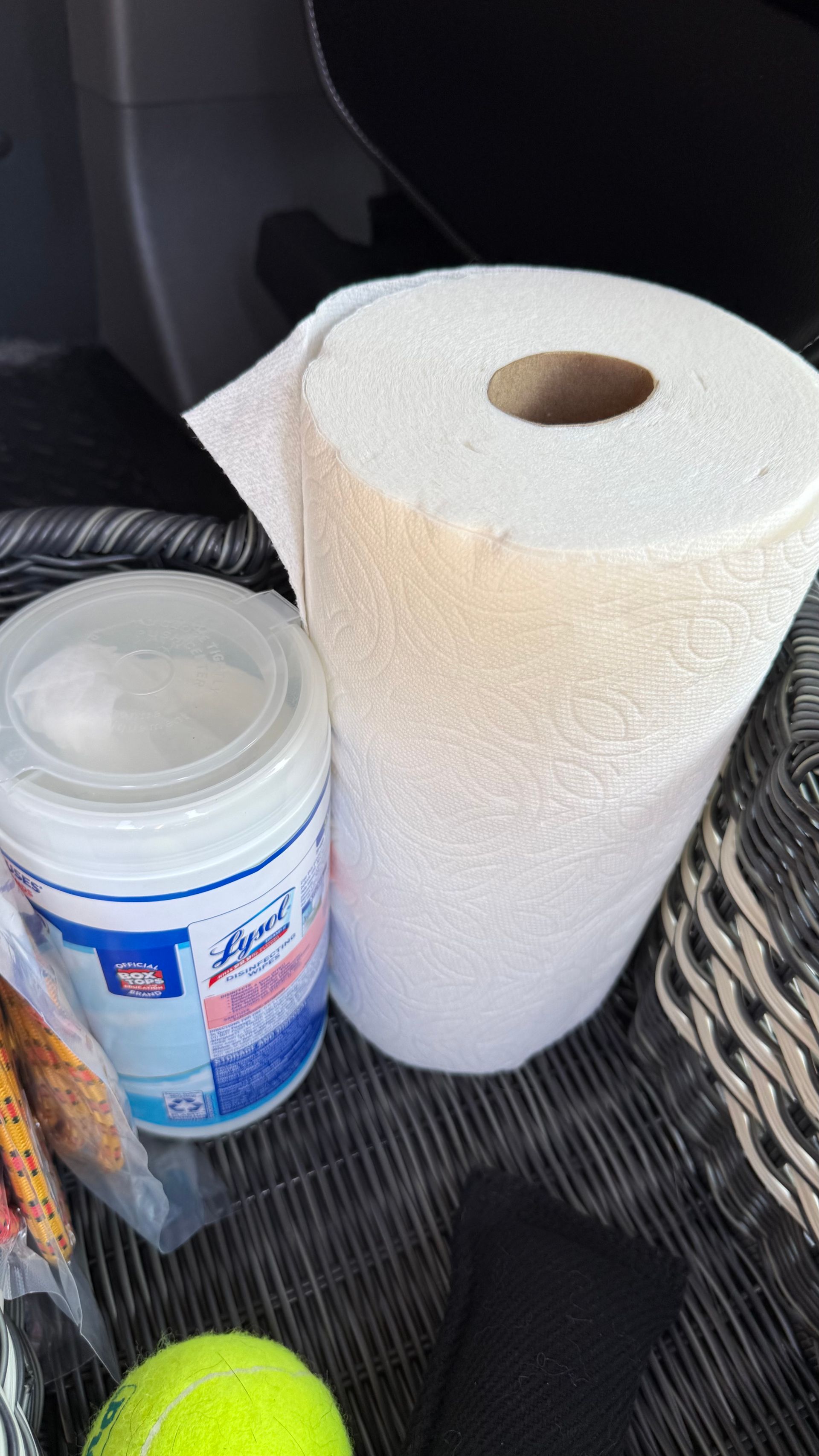 A roll of paper towels is sitting next to a can of wipes and a tennis ball.
