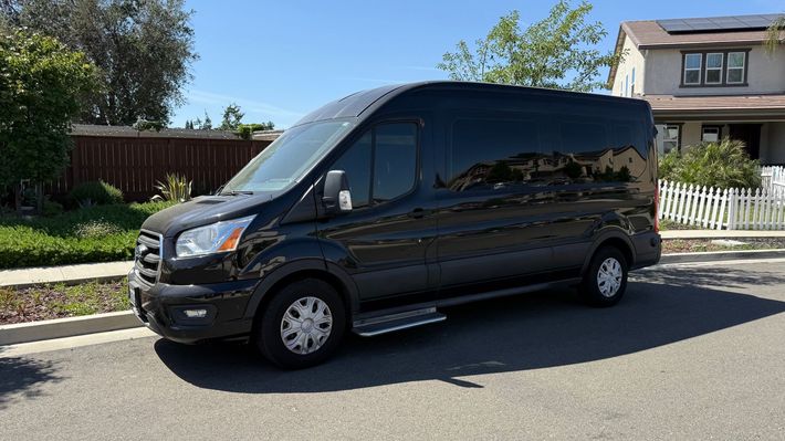A black van is parked on the side of the road in front of a house.