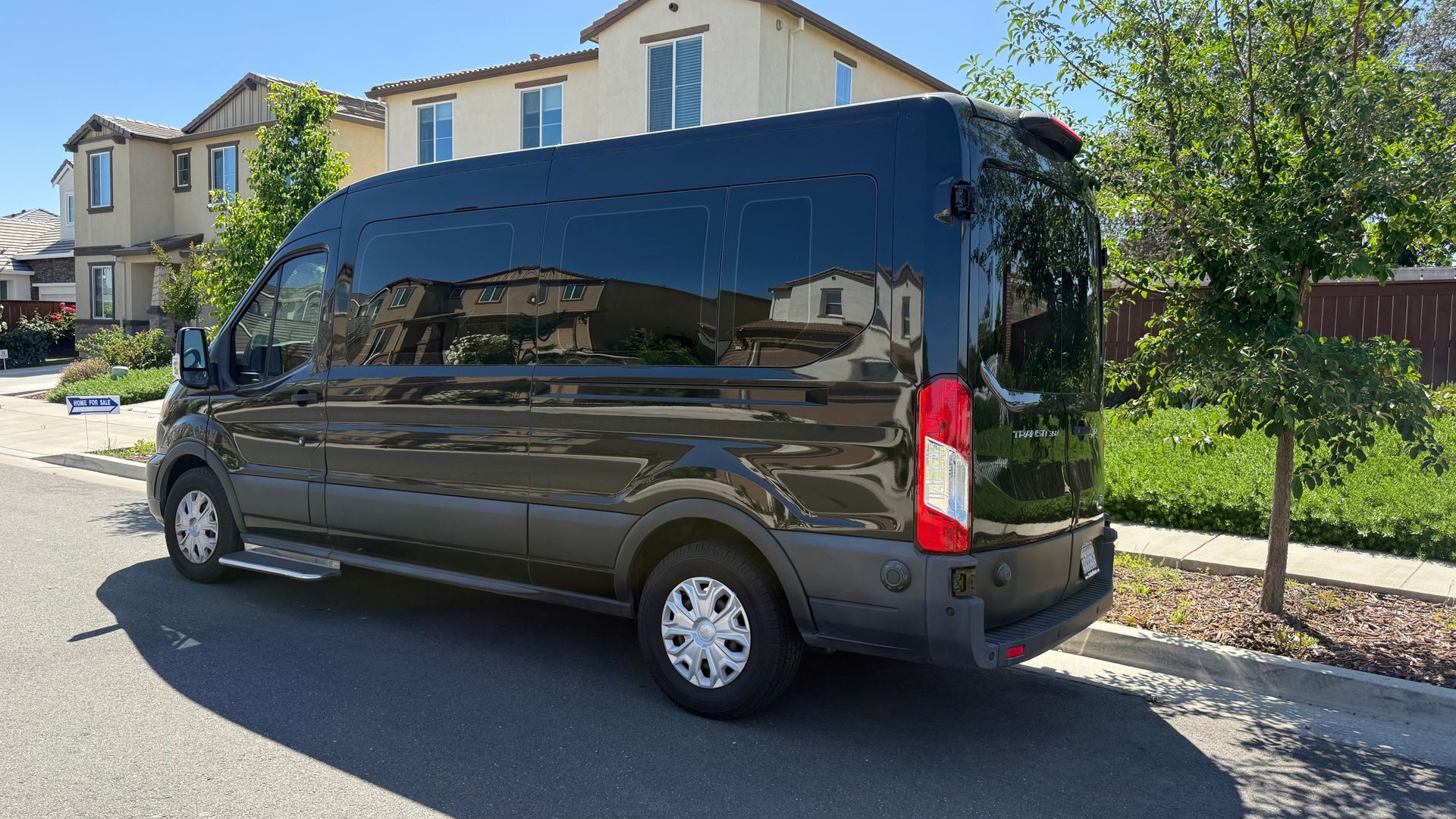 A black van is parked on the side of the road in front of a house.