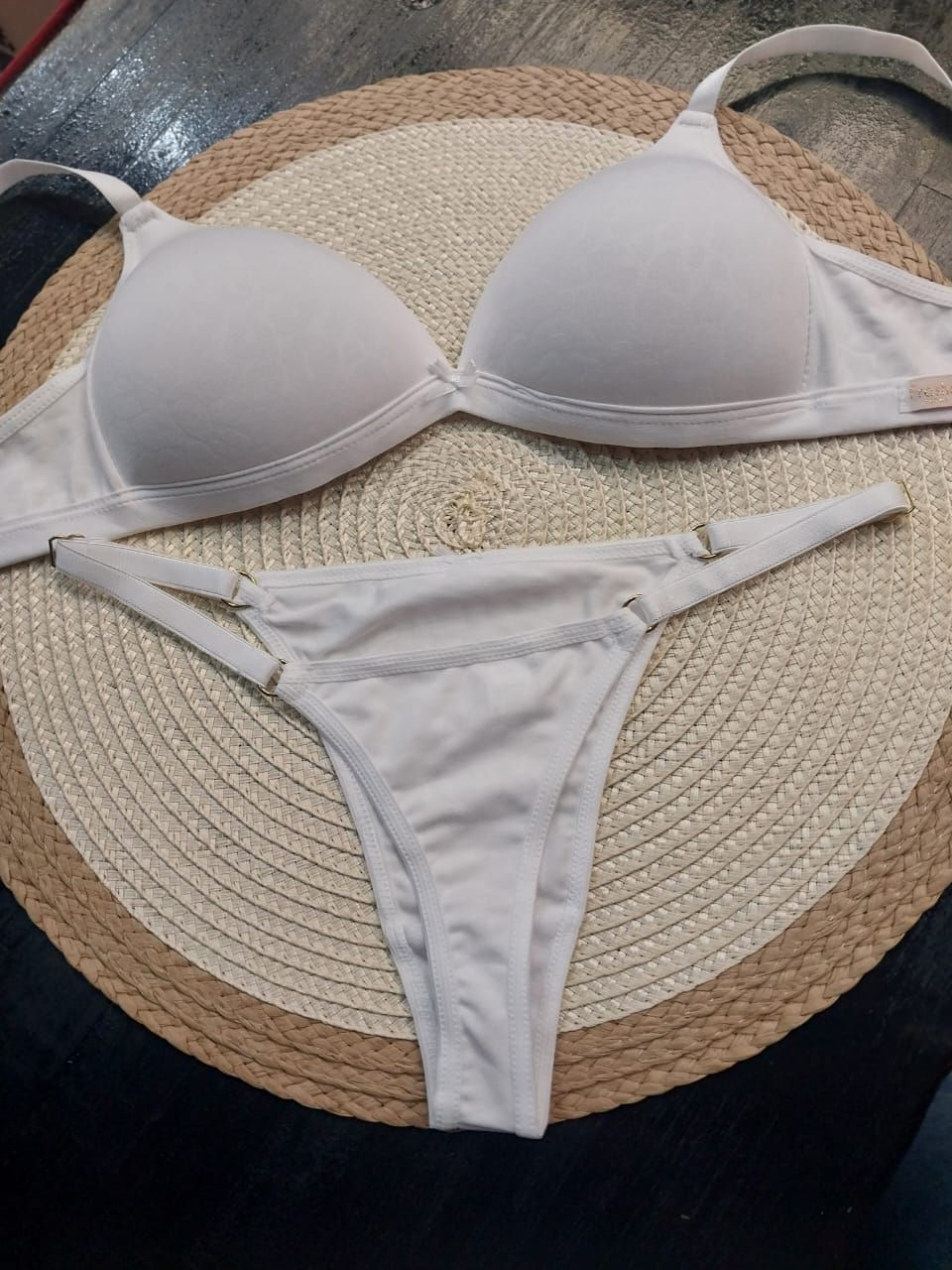 Conjunto de lencería de sujetador y tanga de color blanco sobre mantel redondo tejido de color beige.
