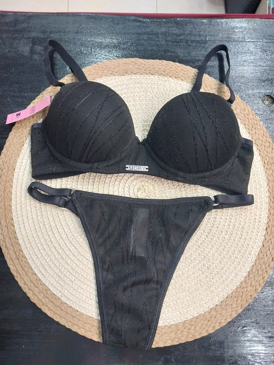 Conjunto de lencería negra: sujetador con relleno y tanga sobre tapete tejido.