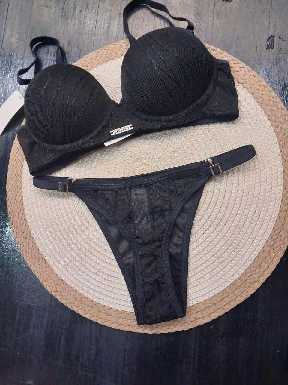 Conjunto de lencería negra sobre una estera tejida. Incluye sujetador y tanga.