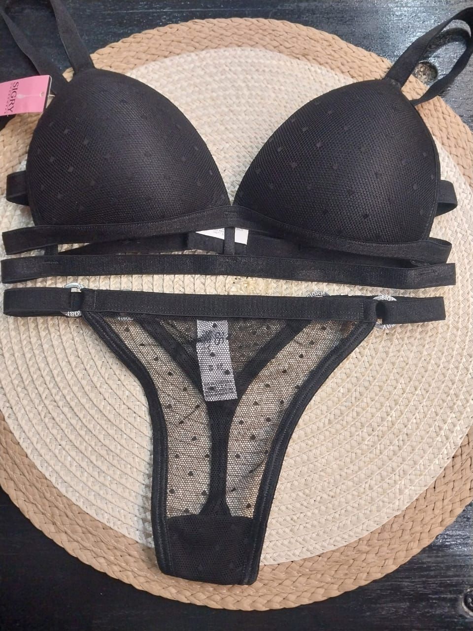 Conjunto de bikini negro con top triangular y detalles de tiras, dispuesto sobre una estera tejida en tonos beige y marrón.