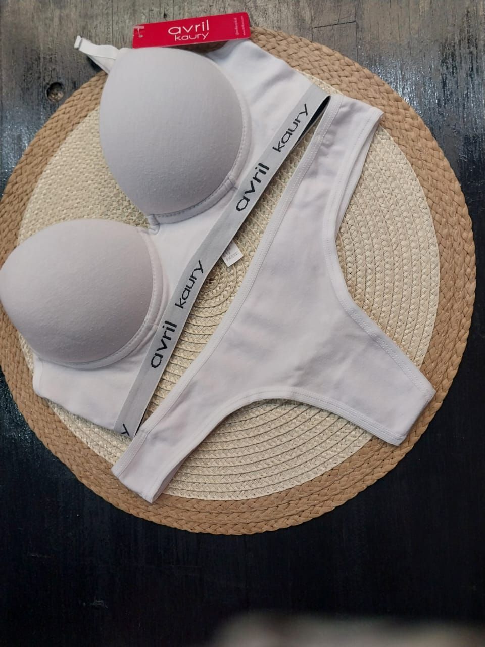 Conjunto de lencería blanca, sujetador con relleno, tanga, con nombre de marca sobre tapete tejido.