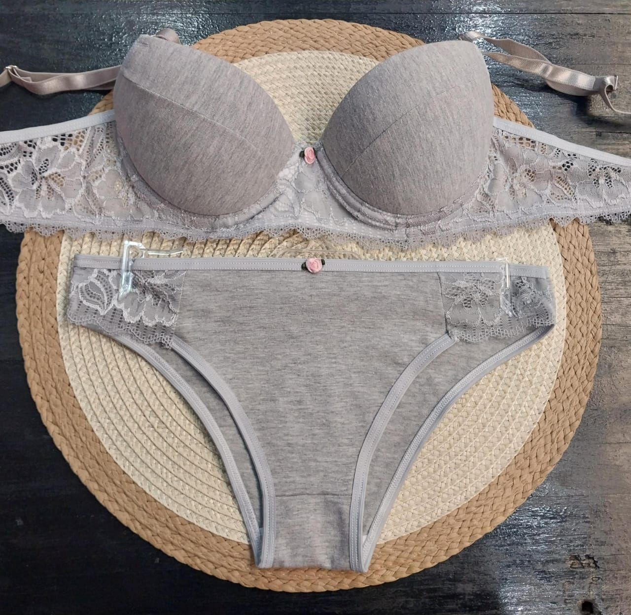 Conjunto de sujetador gris y ropa interior a juego sobre tapete tejido redondo.