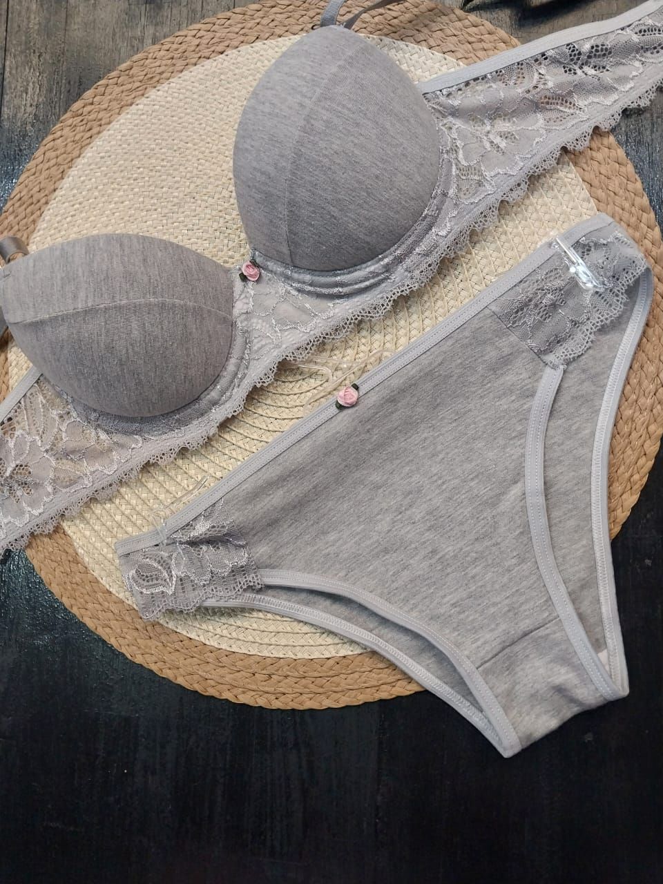 Conjunto de sujetador gris y ropa interior a juego sobre tapete tejido redondo.