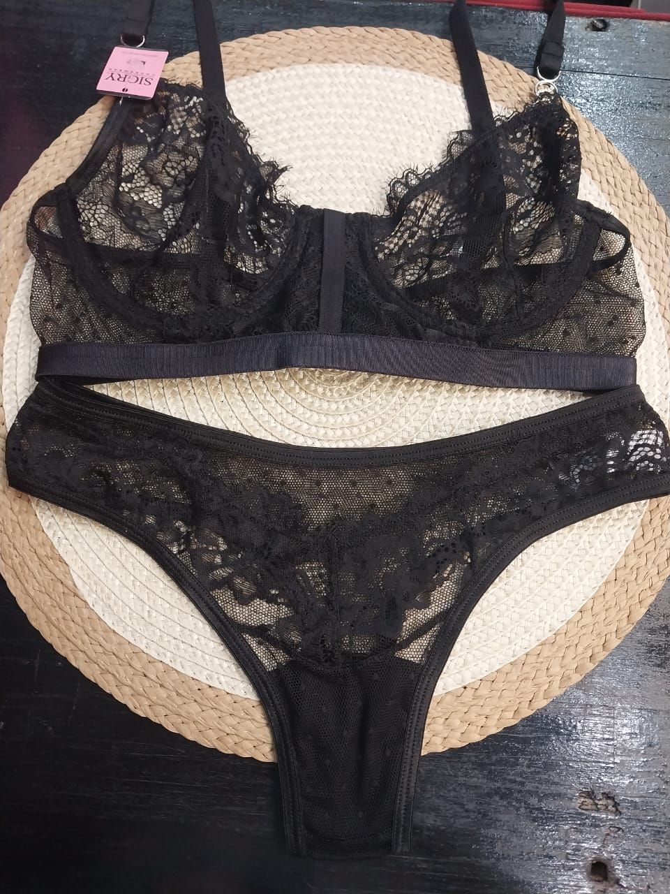 Conjunto de sujetador y bragas de encaje negro sobre una alfombra circular de color tostado y marrón.