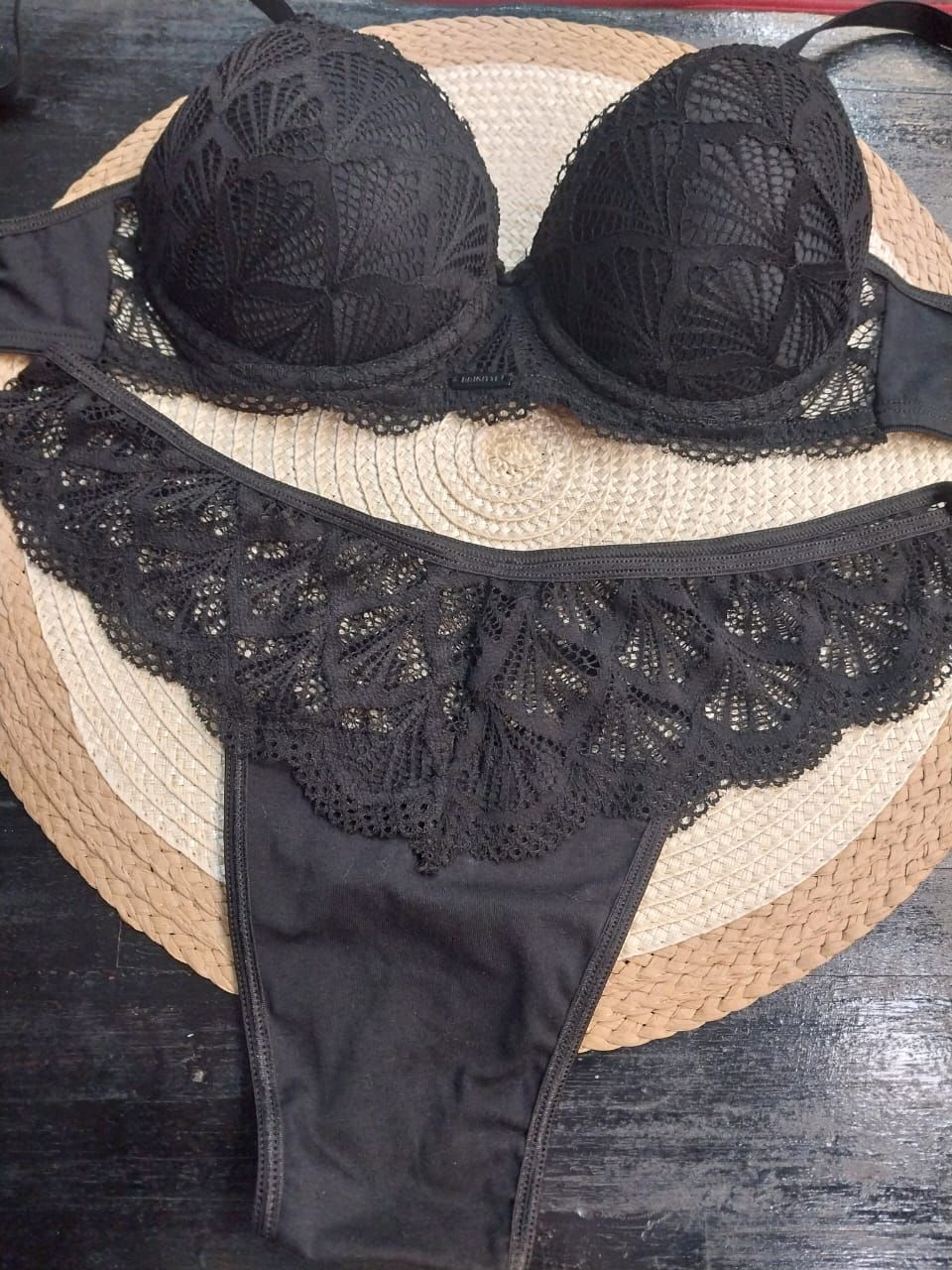 Conjunto de sujetador de encaje negro y ropa interior a juego, apoyado sobre una estera de color beige y marrón.