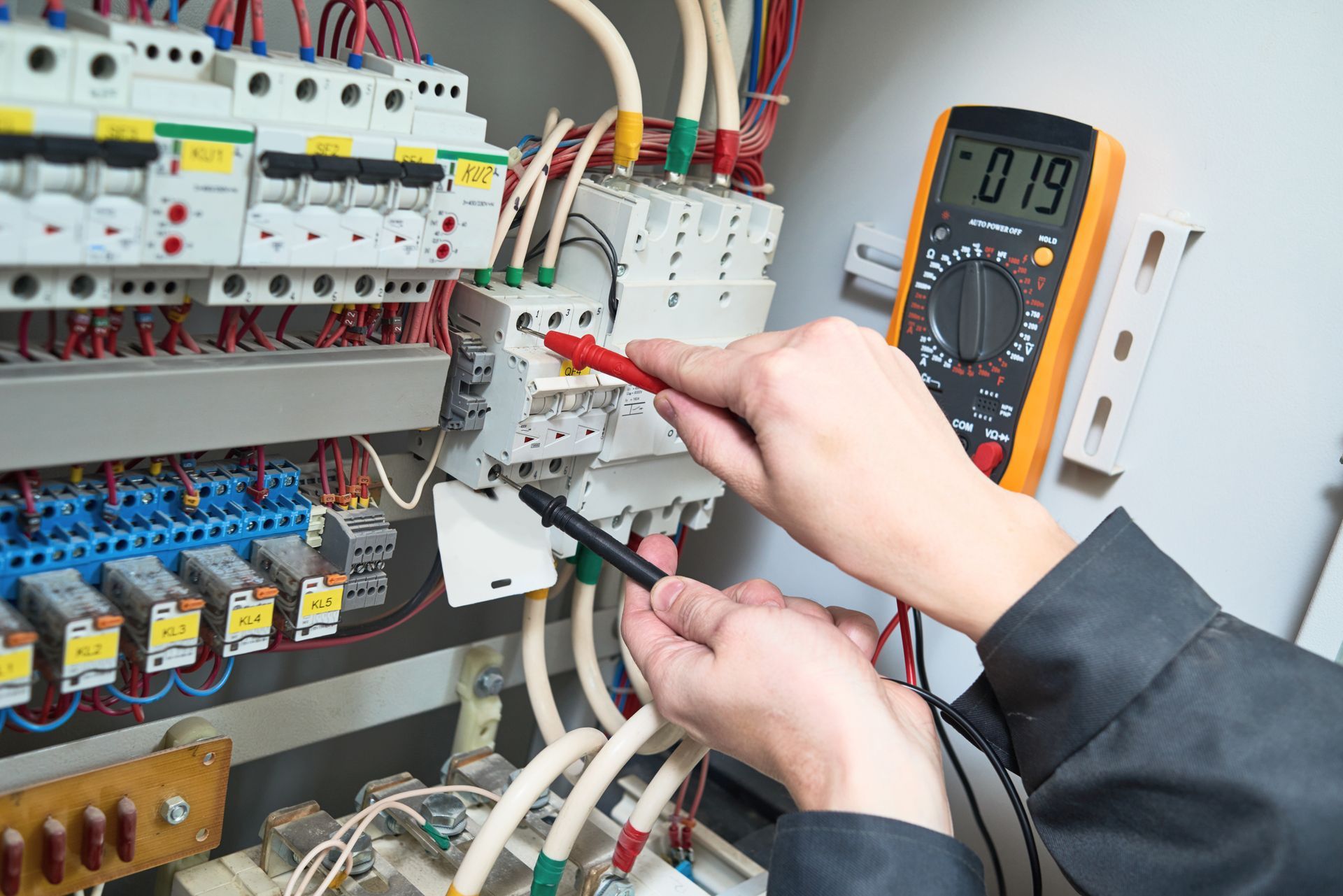 Electrician using a multimeter tester to take measurements in a control panel.