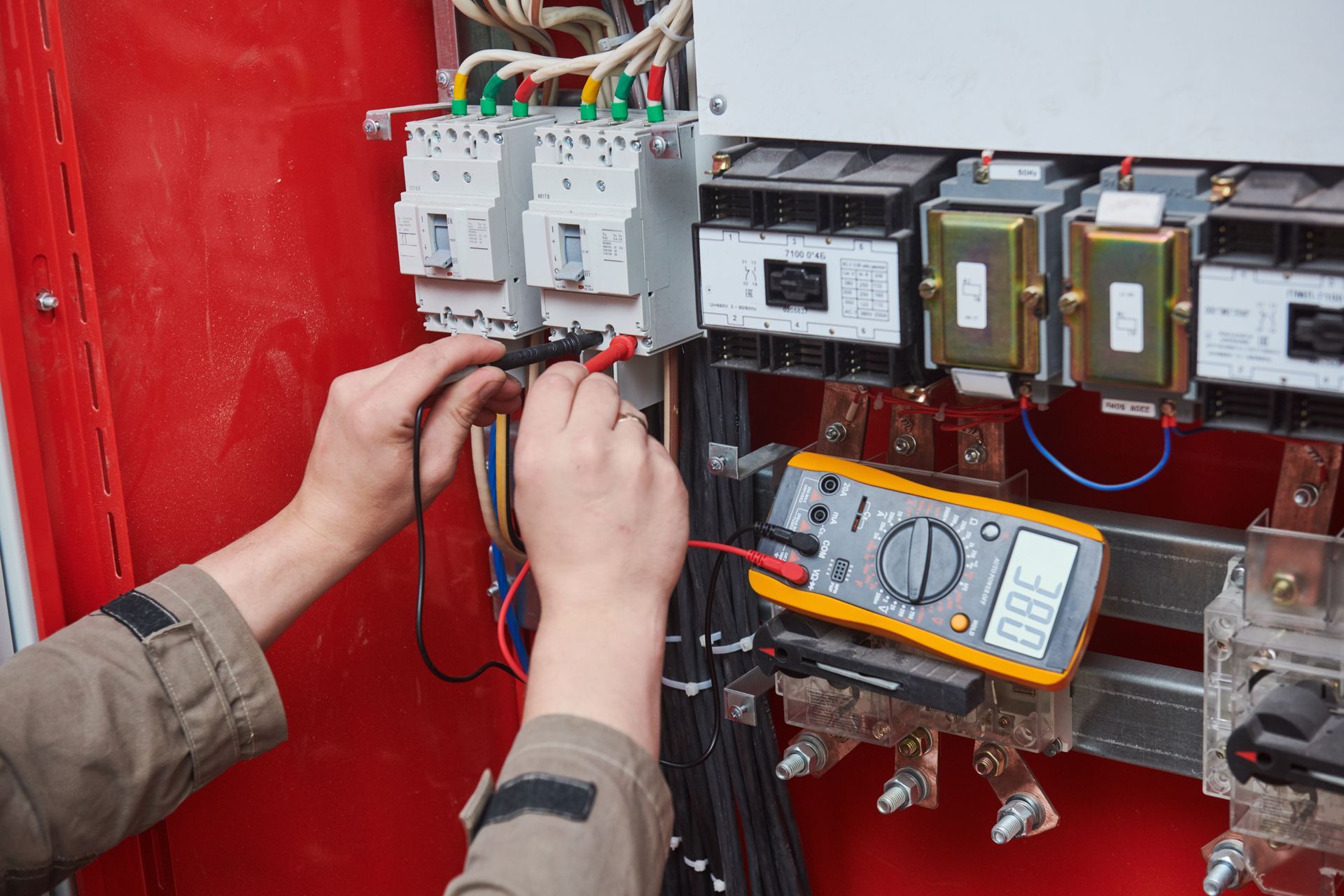 Electrician using a multimeter tester to measure voltage in a control panel.