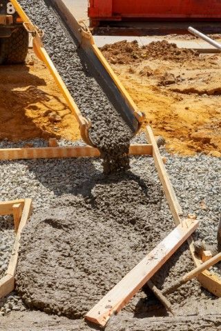Concrete being poured into wooden frame. Construction site with grey concrete and brown wood.