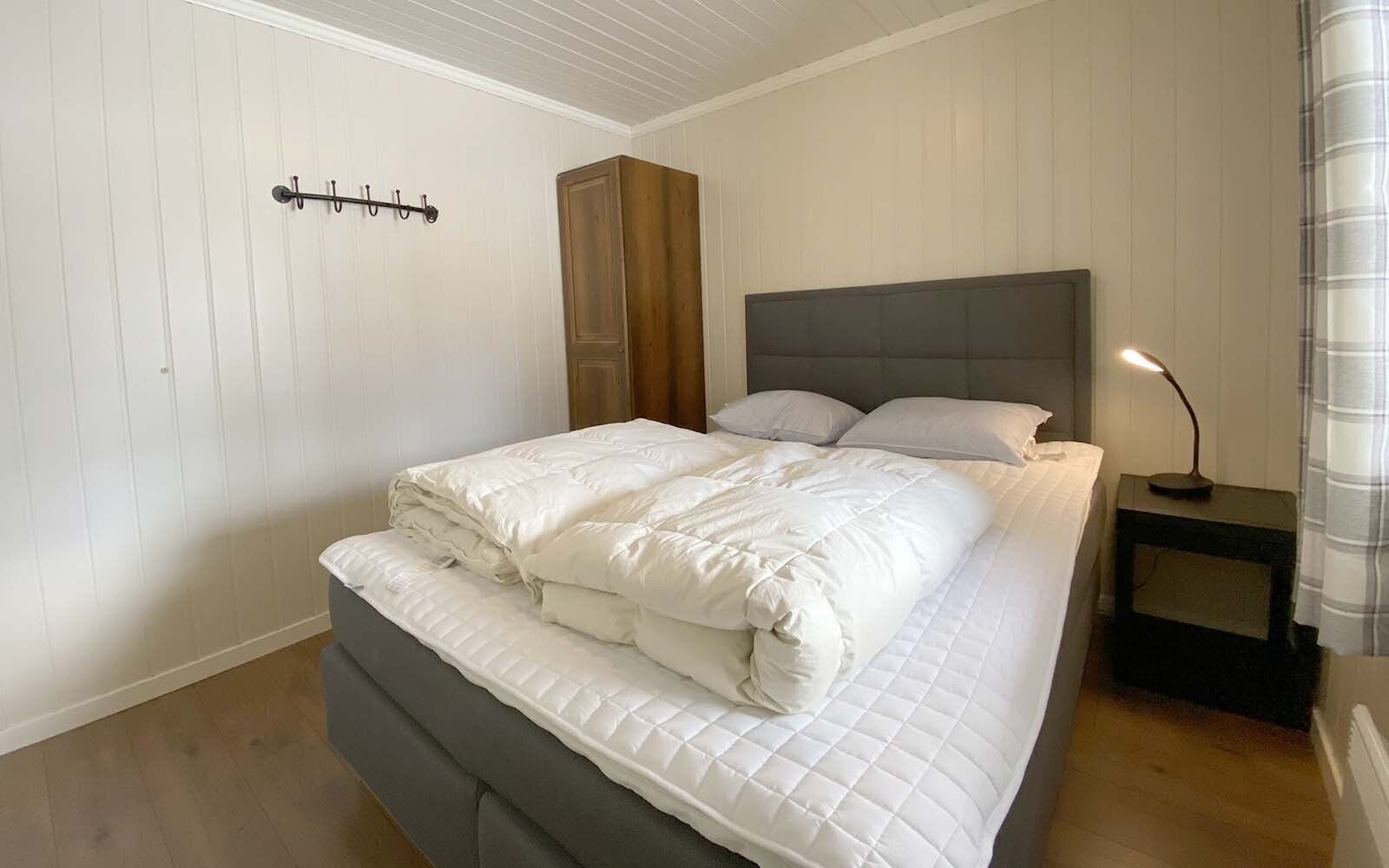 Et soverom med seng, nattbord, lampe og garderobeskap.