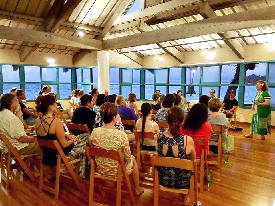 A group of people are sitting in a room with a woman standing in front of them