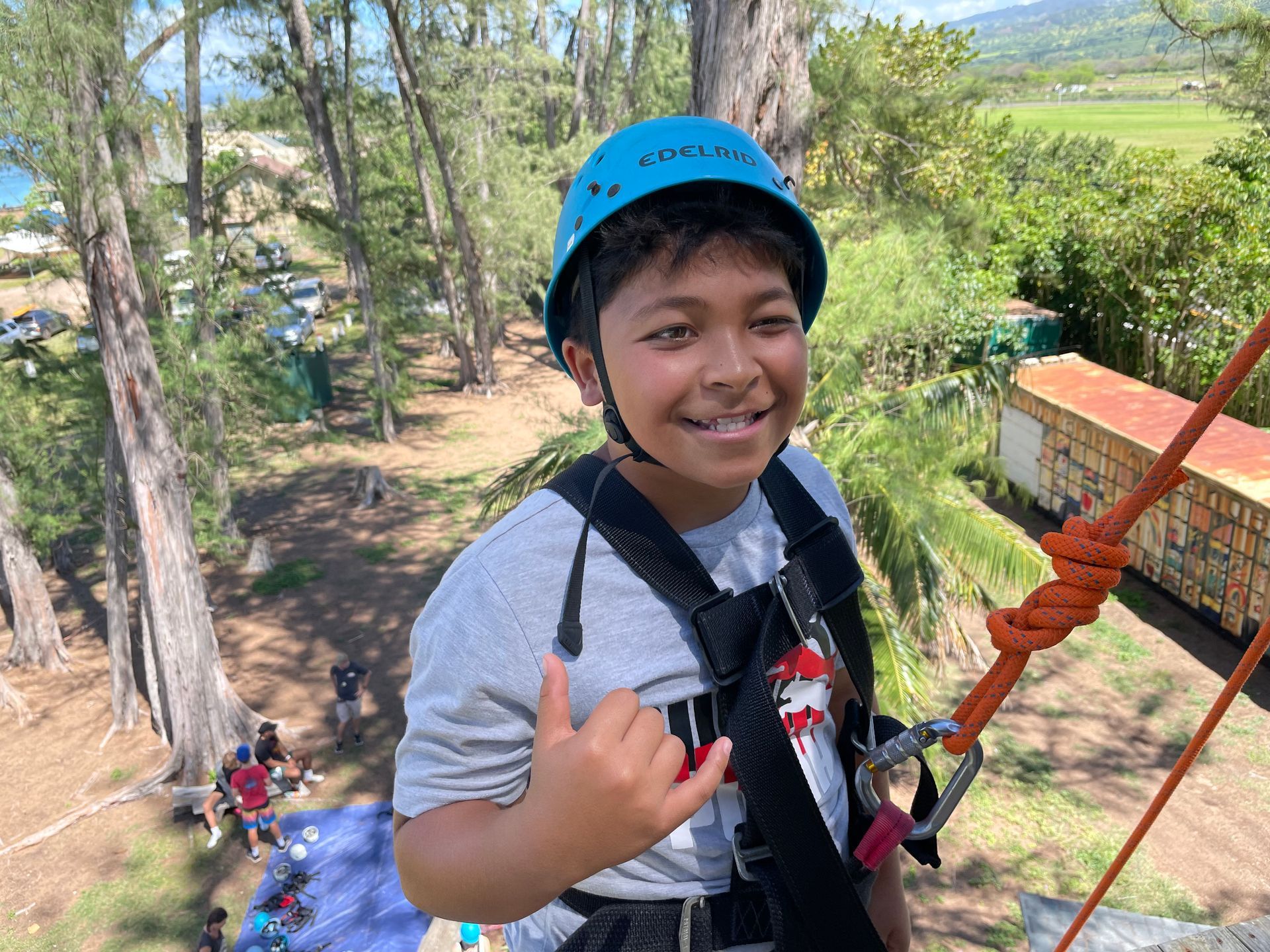 A young boy wearing a helmet and a harness is standing on a rope.
