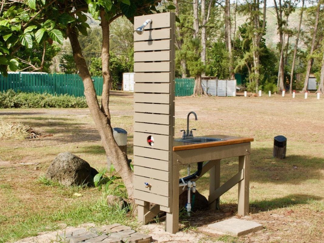 A wooden table with a sink and a shower in the middle of a field.