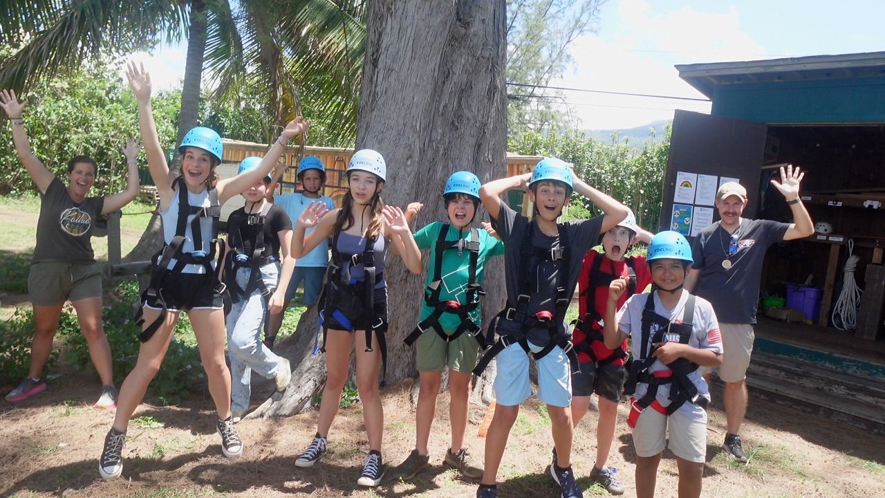 A group of children wearing helmets and harnesses are posing for a picture.