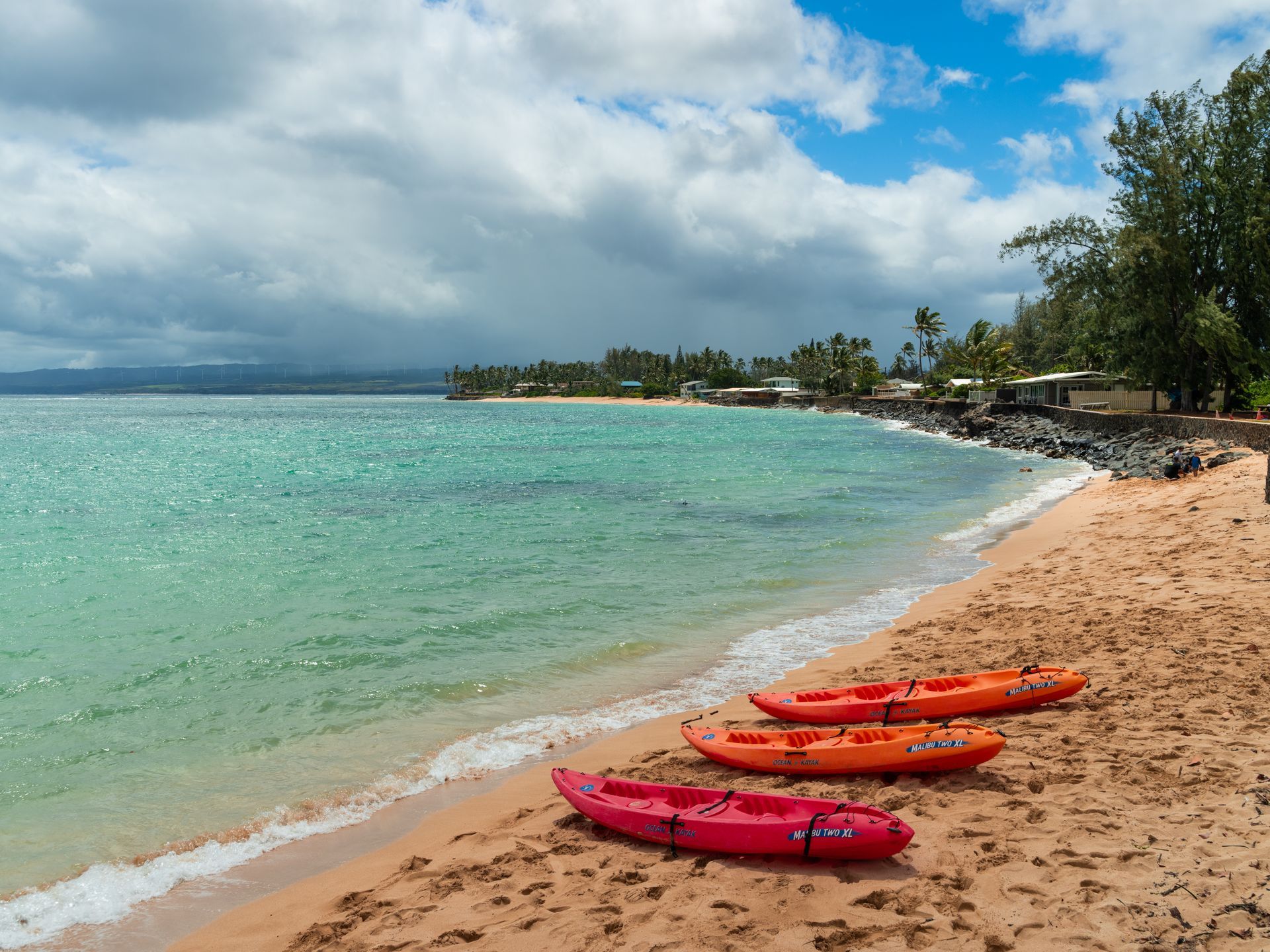 Three red kayaks are sitting on a sandy beach near the ocean.