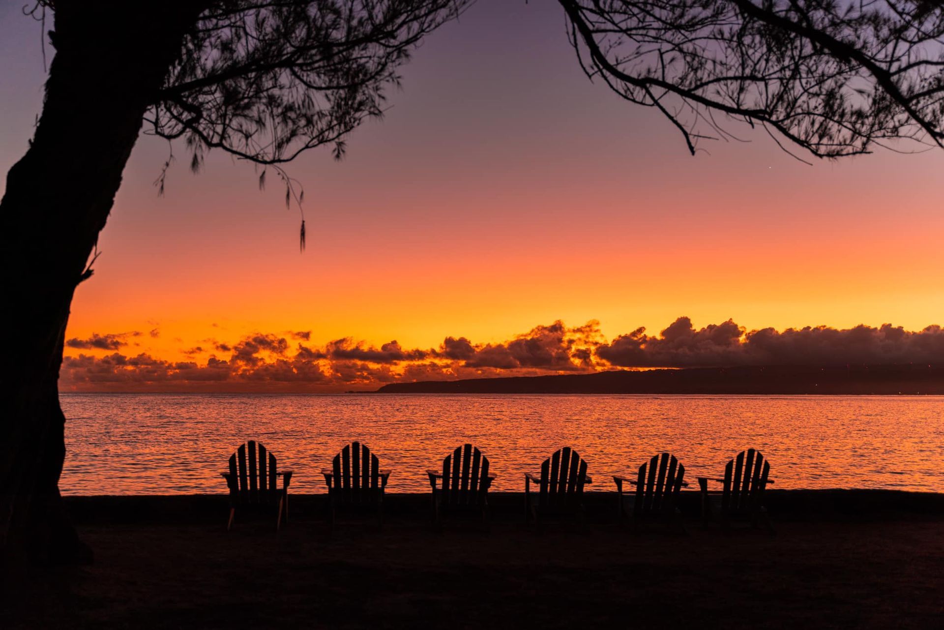 A sunset over a body of water with a row of chairs in the foreground.