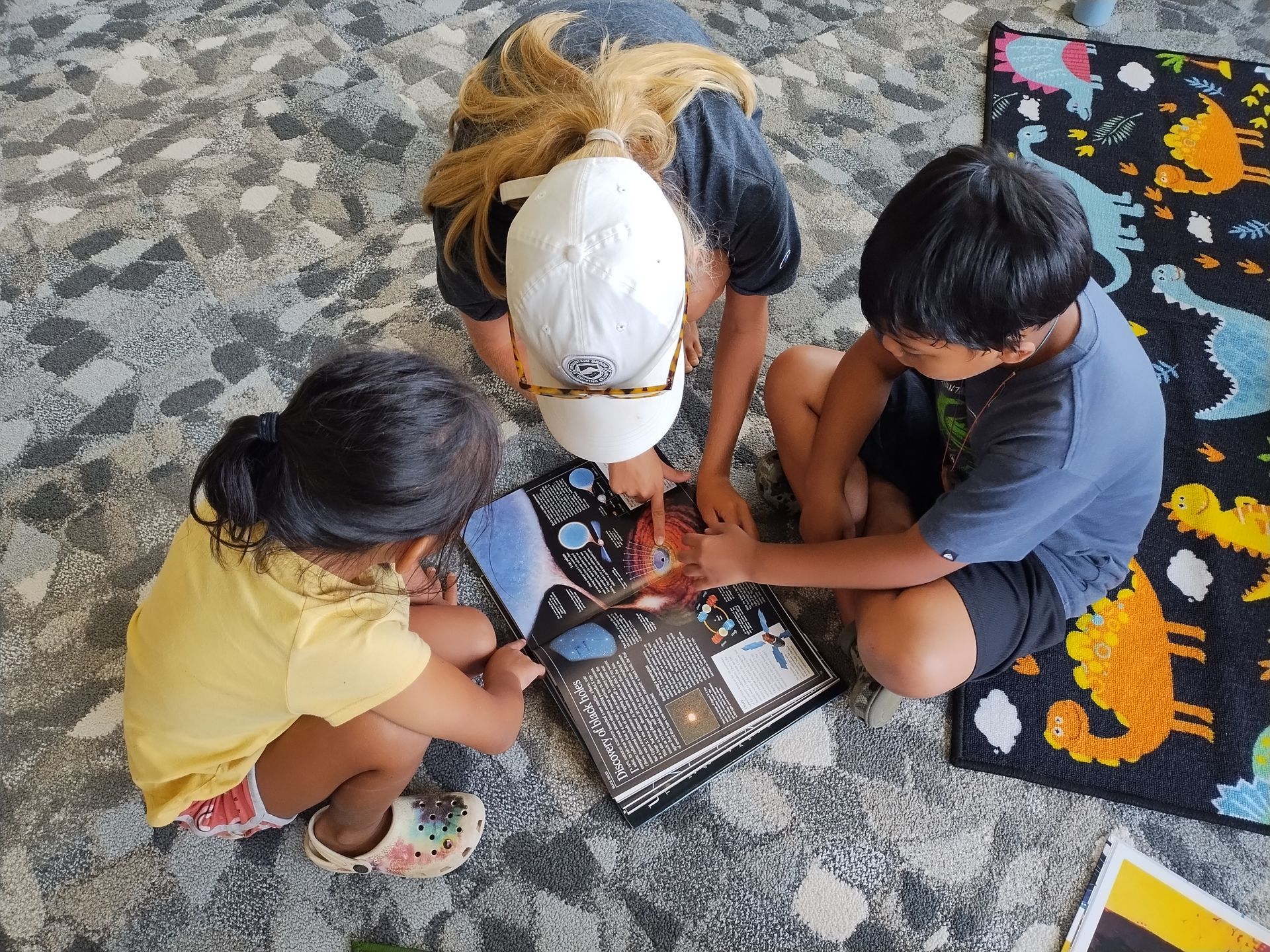Three children are sitting on the floor reading a book.