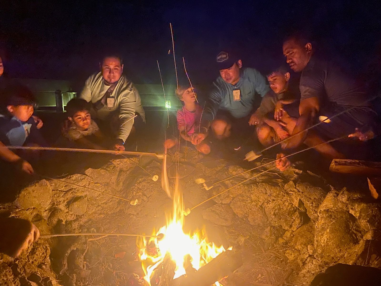 A group of people are sitting around a campfire at night.