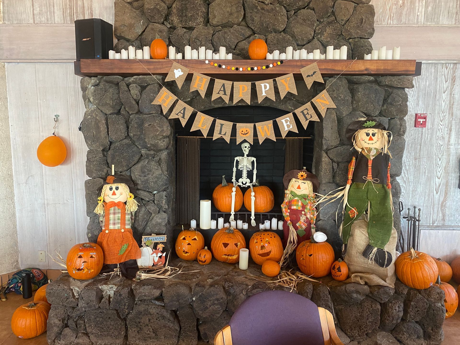 A fireplace decorated for halloween with pumpkins , scarecrows and a skeleton.