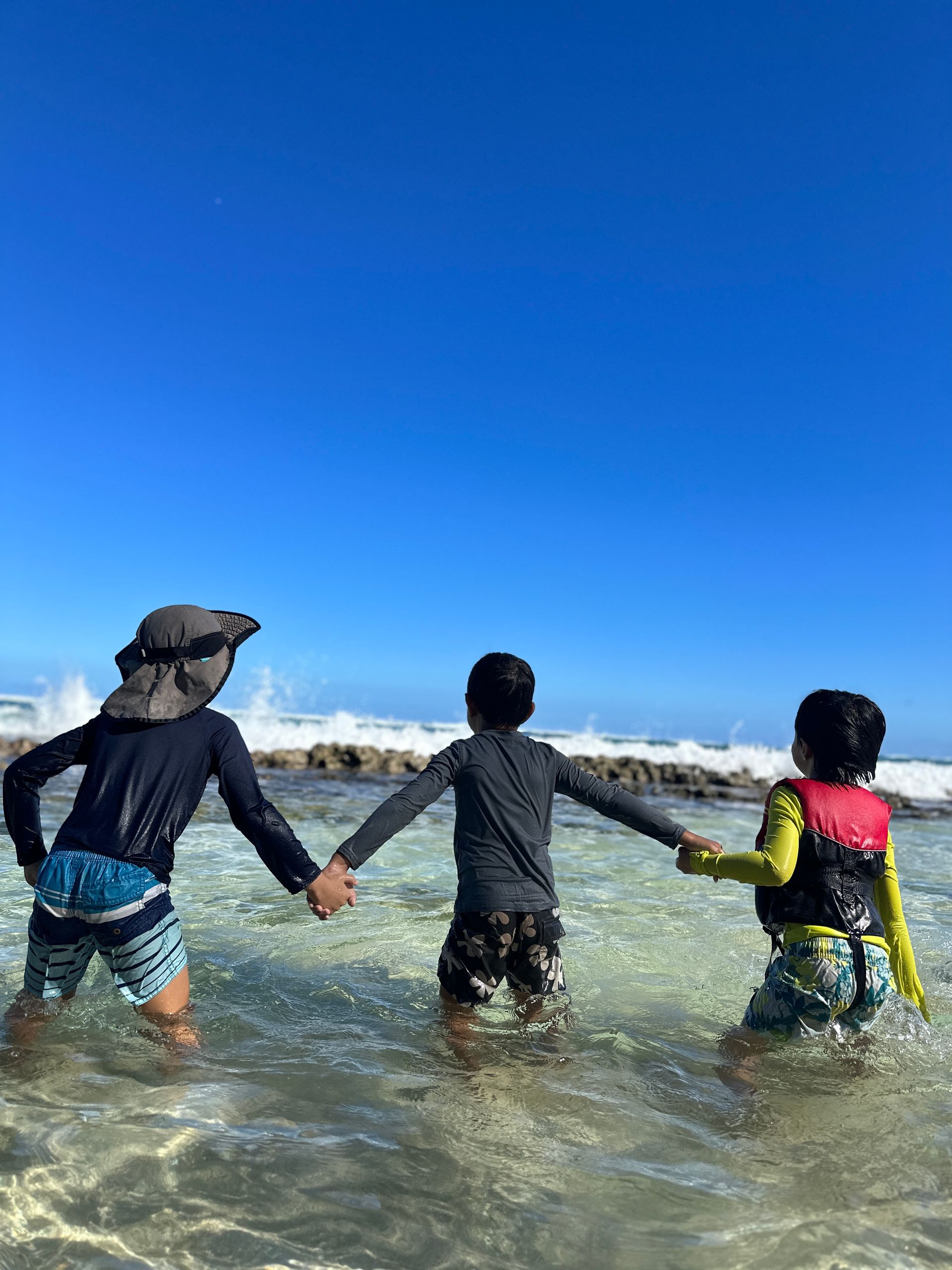 Three children are holding hands in the ocean.