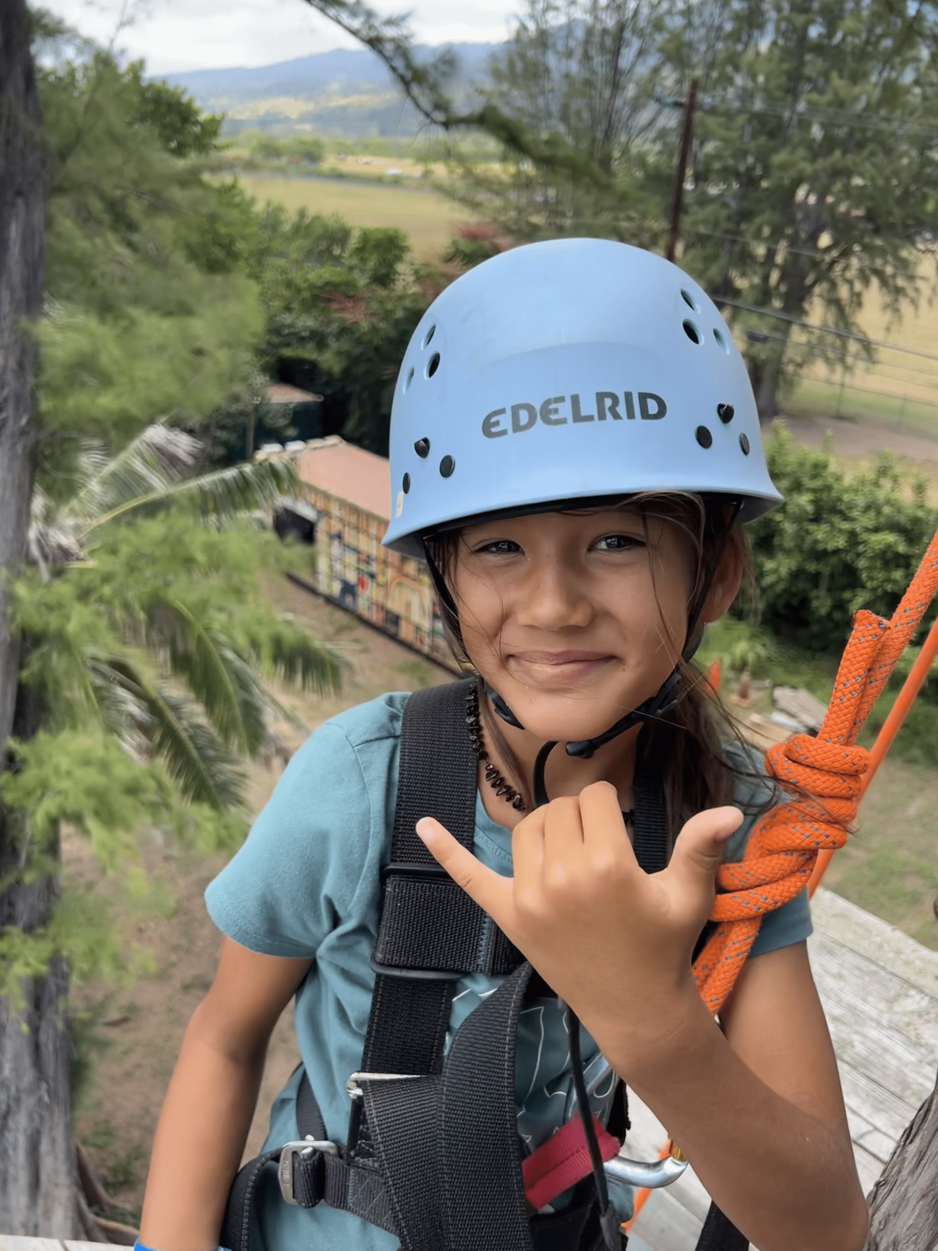 A young girl wearing a blue helmet and holding a rope is smiling.