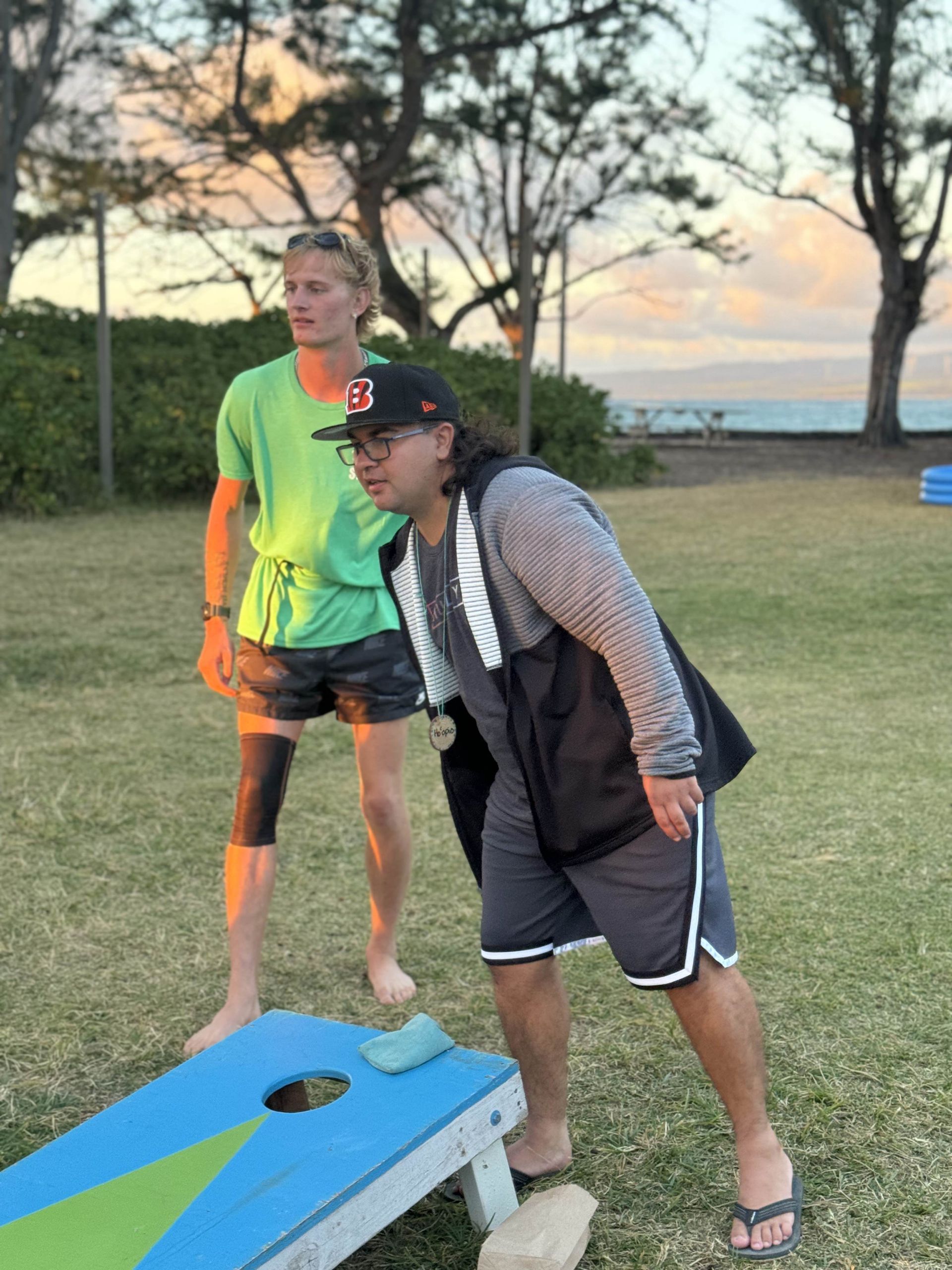 Two men are playing a game of cornhole in a park.