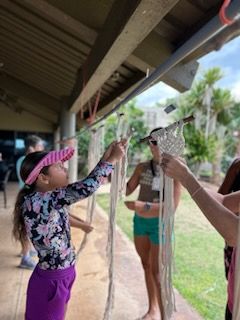 A girl in a floral shirt and purple shorts is holding a rope.