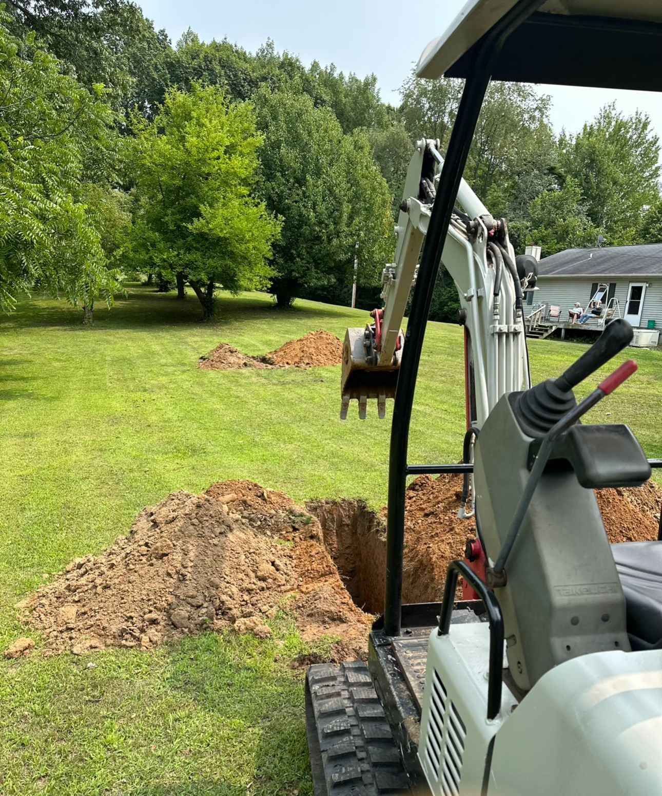 A small excavator is digging a hole in a grassy field.