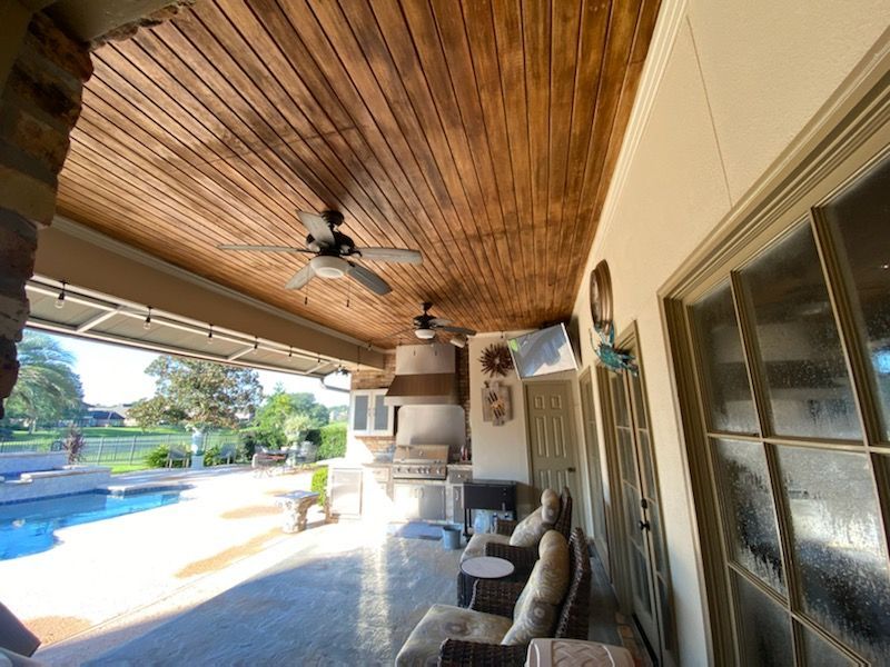 A patio with a wooden ceiling and a ceiling fan.