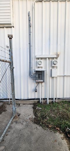 A white building with a chain link fence and electrical outlets on the side.