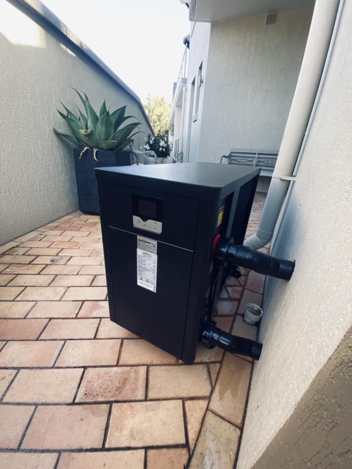 Black Pool Heat Pump on Brick Patio Next to a White Wall — Tempshift Pool Heating in Wyong, NSW