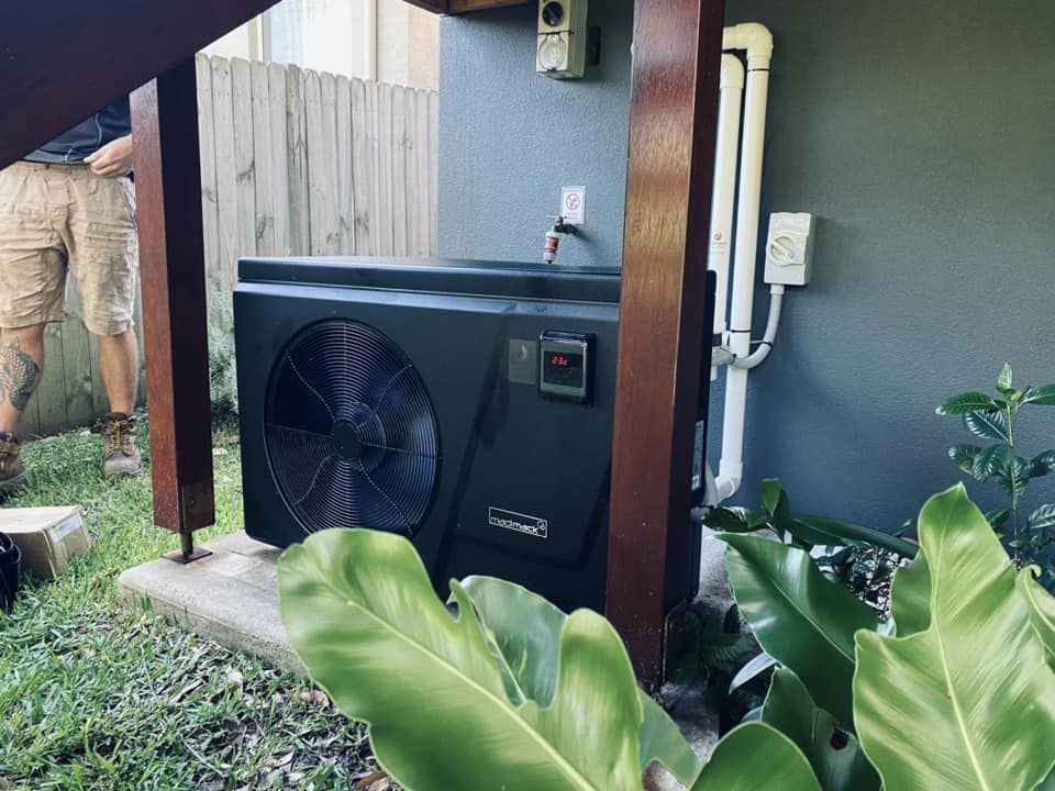 A Dark-Coloured Pool Heat Pump Against a Grey Wall — Tempshift Pool Heating in Wyong, NSW