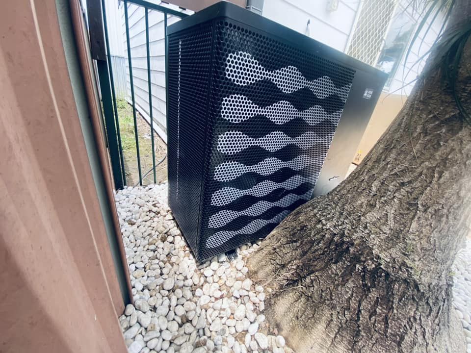 Black Pool Heater Nestled Next to a Tree Trunk, Sitting on White Stones — Tempshift Pool Heating in Gosford, NSW