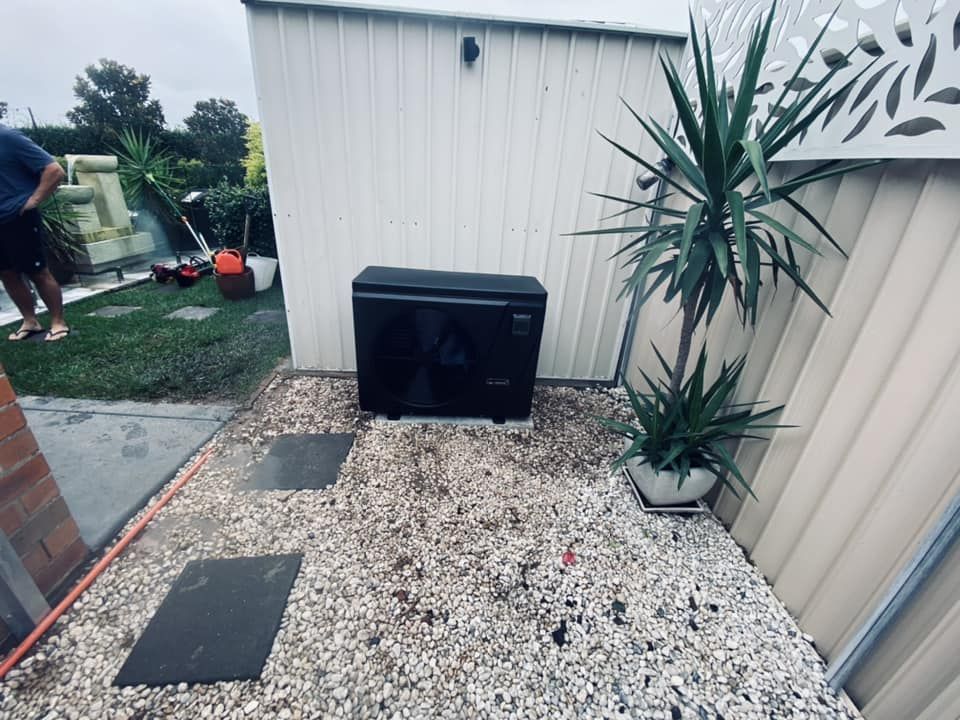 Black Heat Pump on Gravel With Stepping Stones, Next to a Plant and a White Shed — Tempshift Pool Heating in Newcastle, NSW