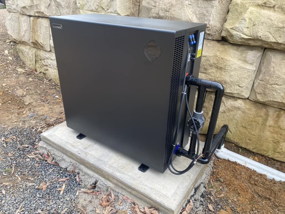 Black Heat Pump on a Concrete Pad Beside a Stone Wall — Tempshift Pool Heating in Hunter Valley, NSW