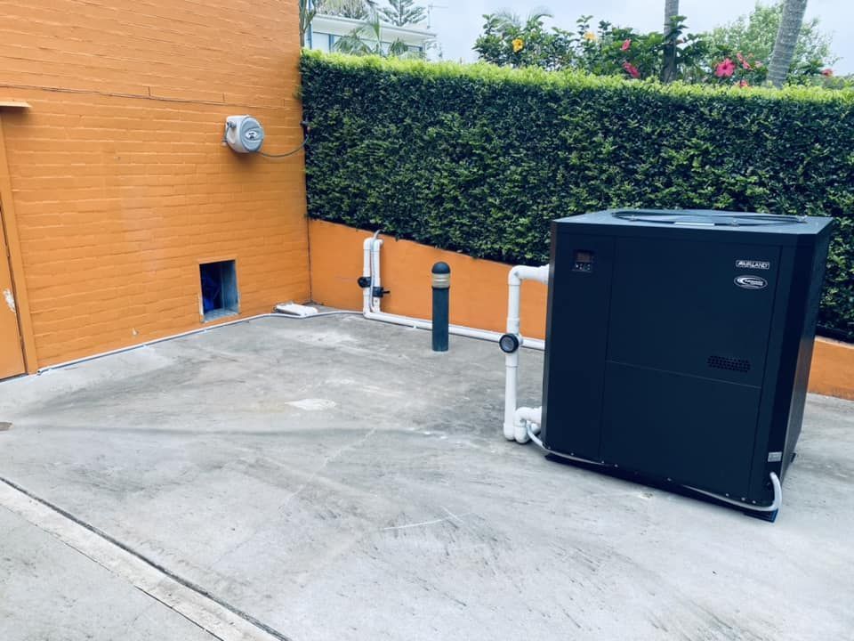 A Black Pool Heater Sits Near a Concrete Wall — Tempshift Pool Heating in Lake Macquarie, NSW