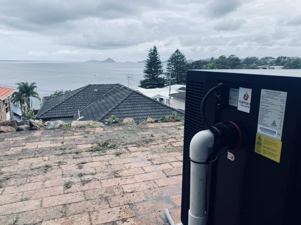 A Dark-Coloured Pool Equipment Overlooks a Coastal Town With a Cloudy Sky — Tempshift Pool Heating in Buff Point, NSW