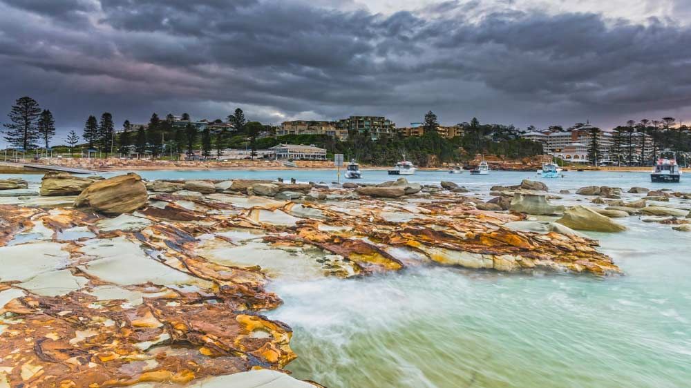 Rocky Coastline With Turquoise Water, Boats, and Buildings — Tempshift Pool Heating in Gosford, NSW